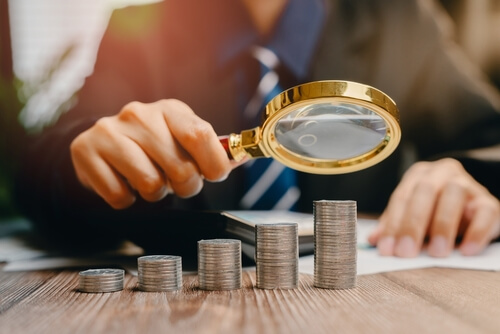 A,Close-up,Of,Businessman,Analyzing,Coins,With,Magnifying,Glass,In